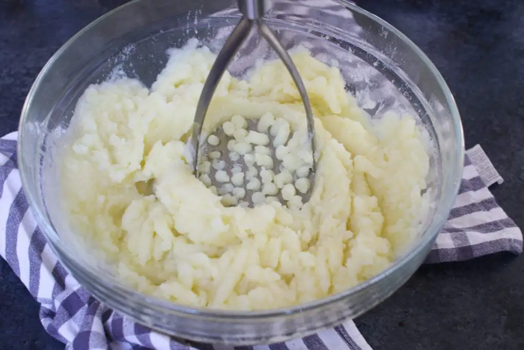 Schiacciate le patate cotte con un masher di patate.