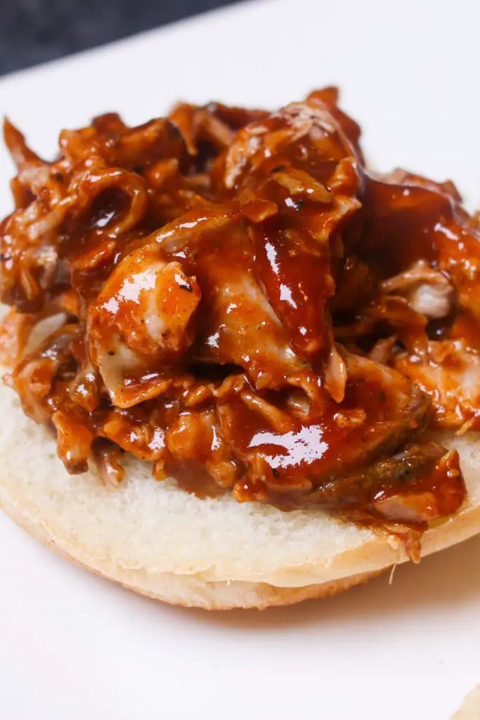 Aggiungi la salsa barbecue al maiale sbriciolato su un panino con hamburger.